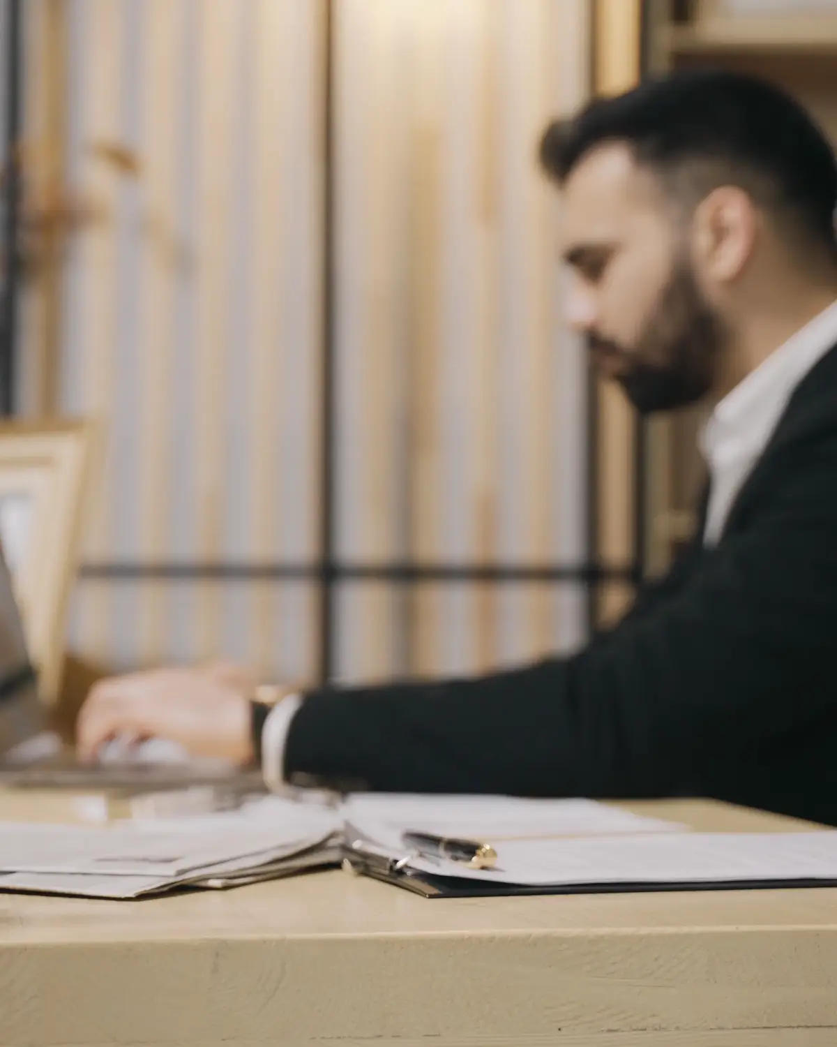 A person in a suit working at a laptop on a wooden desk