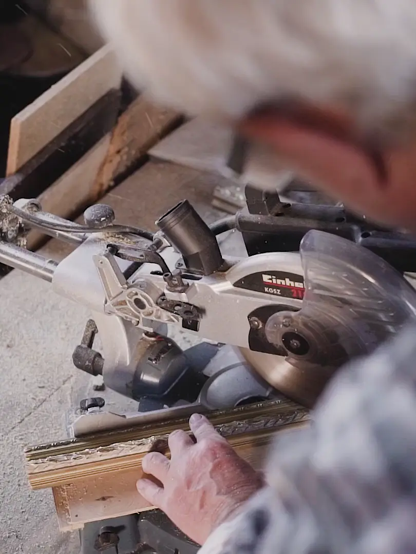 A carpenter cutting a length of moulding on a mitre saw